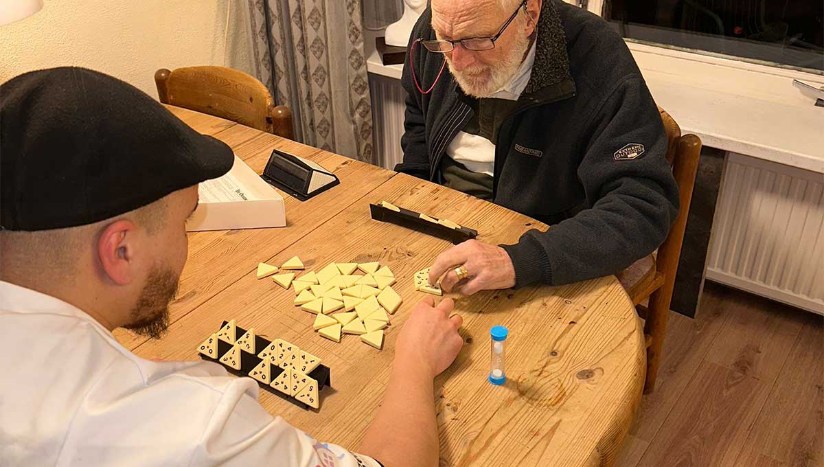 Verpleegkundige speelt een gezelschapsspel met een oudere cliënt tijdens een thuiszorgmoment